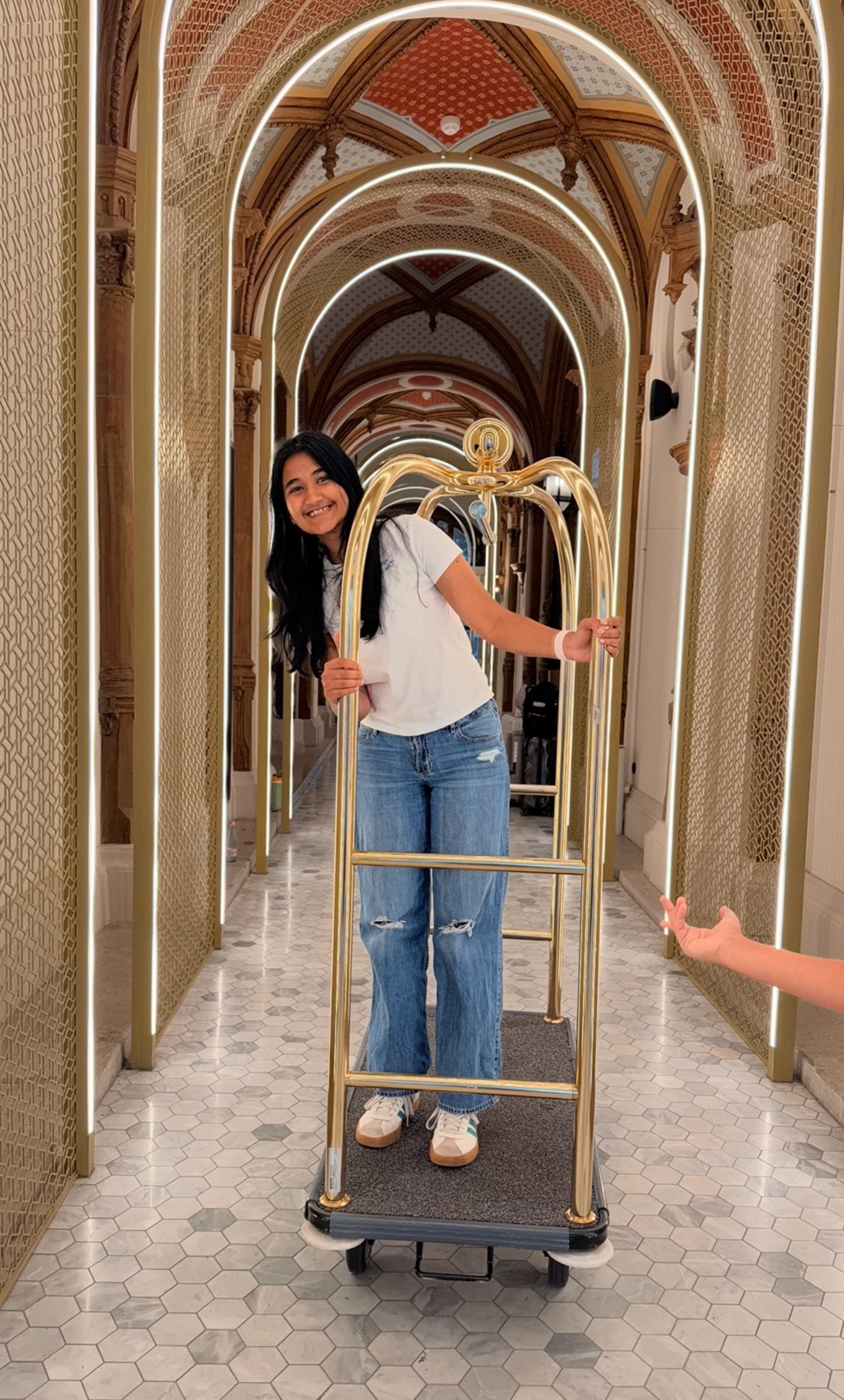 Khushi smiling on a luggage cart in an arched hallway